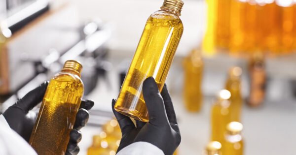 Lean production of cosmetics on factory. Close-up portrait of hands in black rubber gloves holding two bottles with yellow substance looking at quality of made product. Checking done work on factory